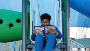 A child reads a Ranger Rick Dinosaurs magazine at the playground, on the slide