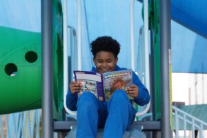 A child reads a Ranger Rick Dinosaurs magazine at the playground, on the slide