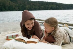 Two children read books on a dock