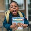 young child with a backpack holding a ranger rick dinosaurs magazine