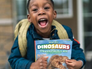 young child with a backpack holding a ranger rick dinosaurs magazine