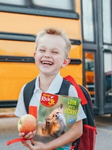 child holding magazine in front of school bus